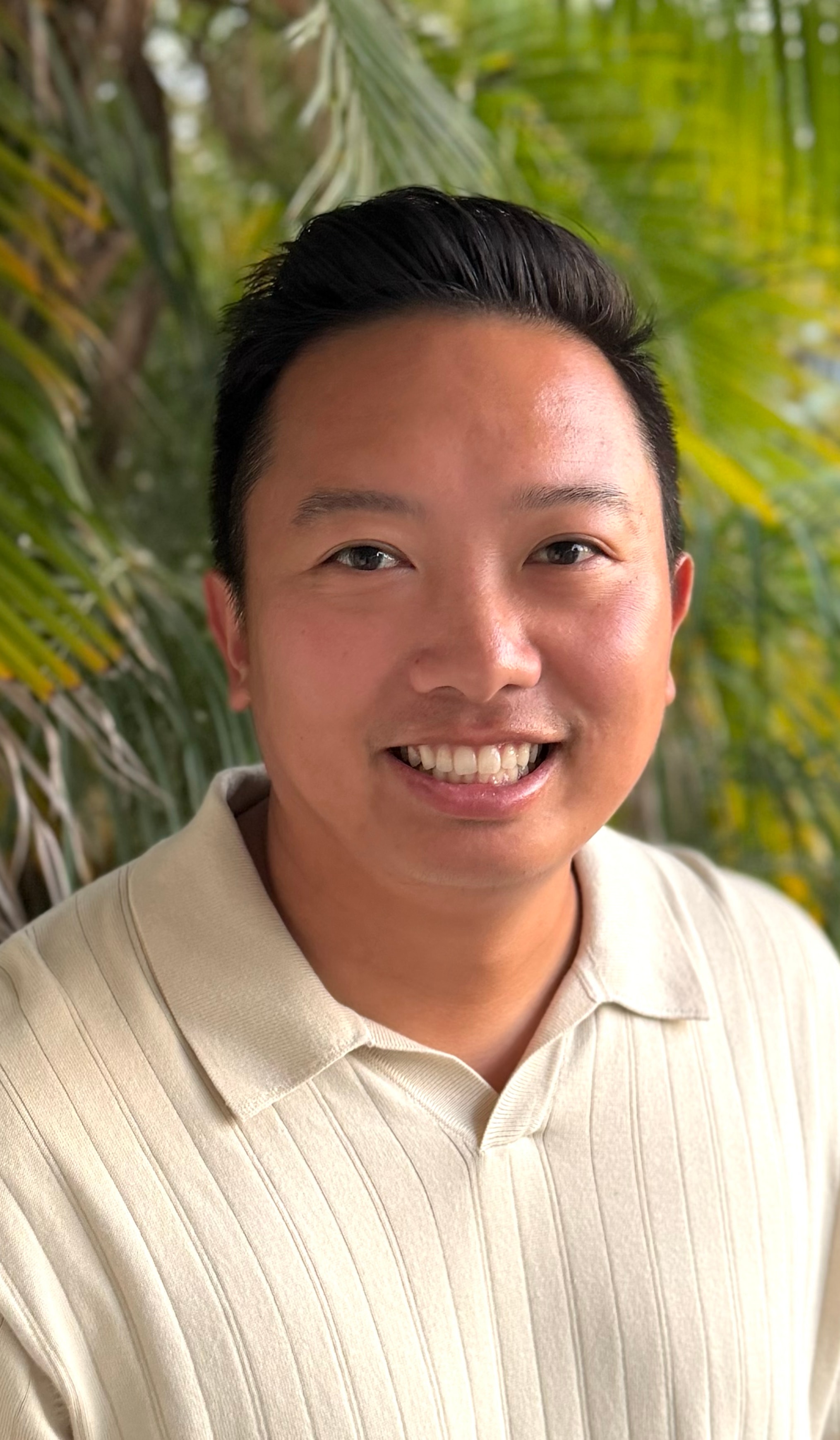 Dr. Binh Pham smiling, outdoors in front of palm foliage